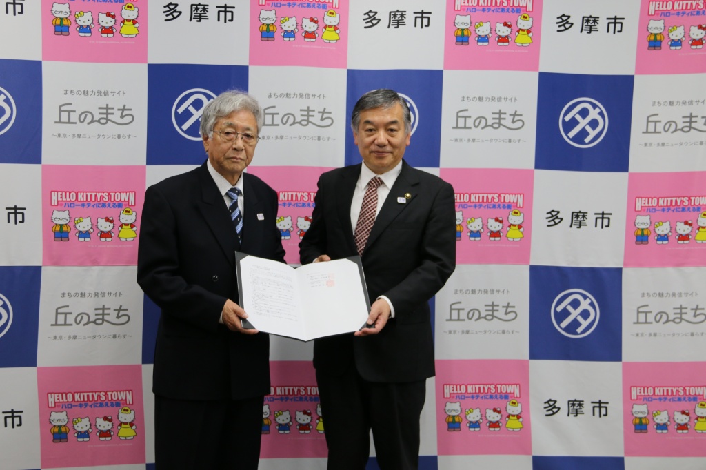 協定書を手に記者らの記念撮影に応じる阿部市長（右）と大澤理事長