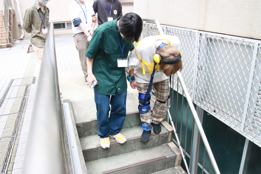 高齢者疑似体験グッズを装着して階段を下りる学生