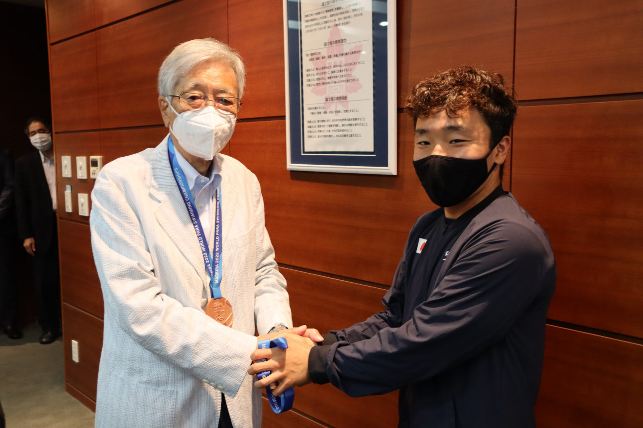 大澤理事長の首にメダルをかけ握手を交わす齋藤選手