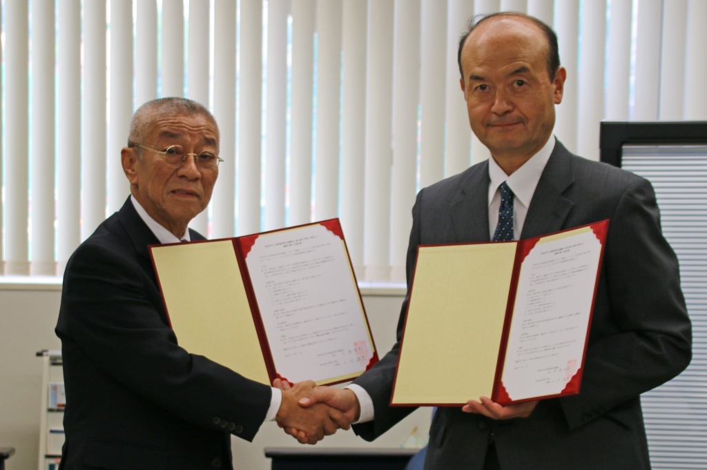 固い握手で相互協力を誓う大塚会長（左）と二川学部長