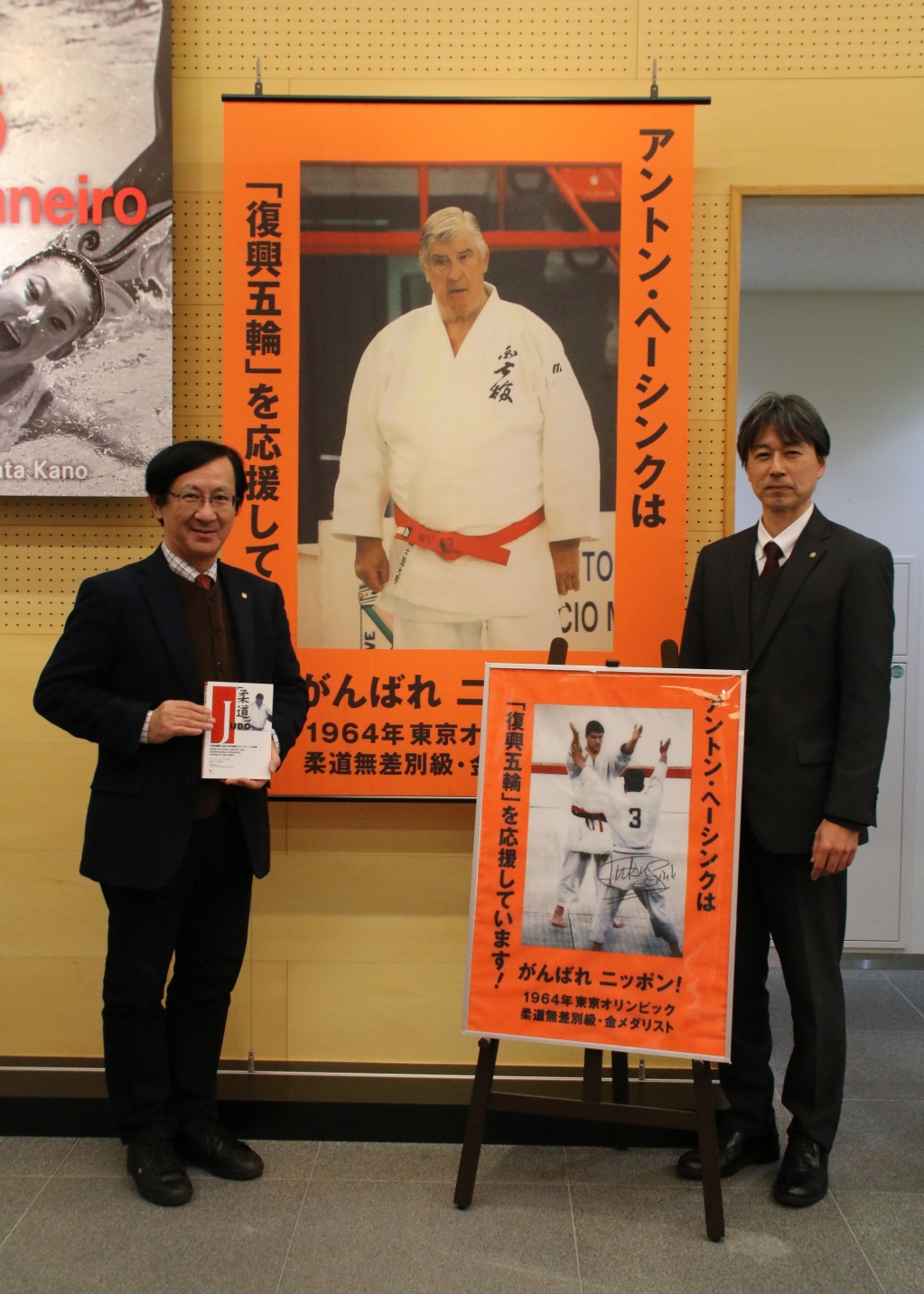 国士舘スポーツの殿堂に設置のポスターとともに。左：佐藤学長、右：永冨教授
